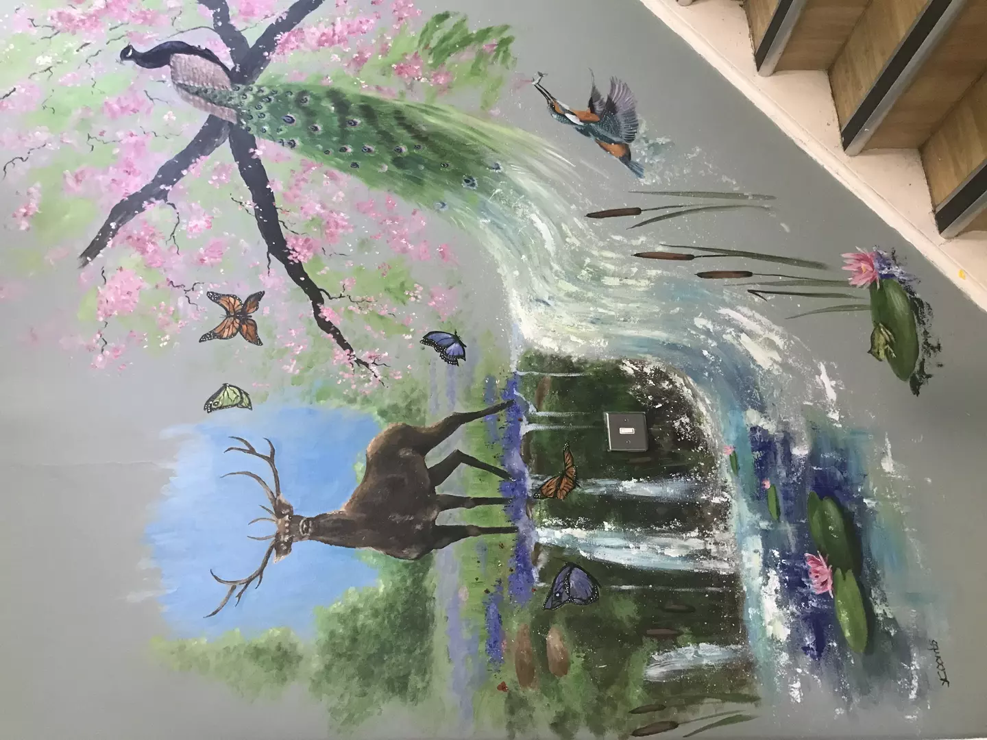 A painting of nature and wildlife, with a peacock perched in a tree and a stag stood in front of a stream.