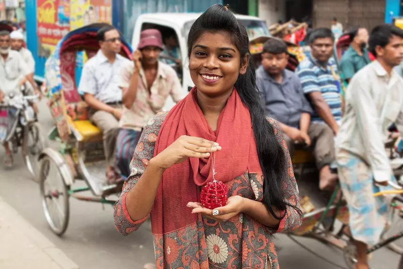 A Bangladeshi woman stands in the street smiling at the camera, holding one of the Christmas decorations and smiling at the camera. 
