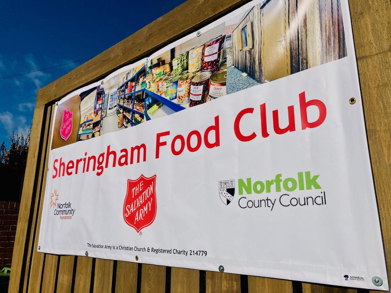 A banner promoting Sheringham Food Club on top of a wood panelled fence.
