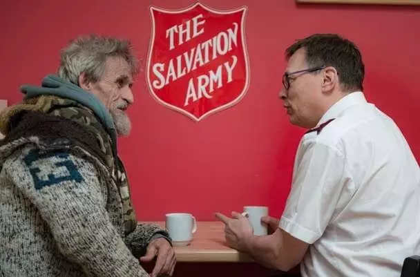 Two people having a conversation at a Salvation Army premises, one older man talking to a younger man in TSA uniform